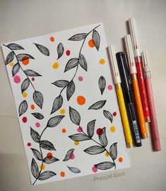 some markers and pens are sitting next to a piece of paper with leaves on it