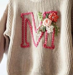 a sweater with flowers on it and the letter m is embroidered into the front, along with other letters that spell out love