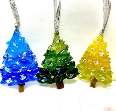 three glass christmas trees are hanging from chains