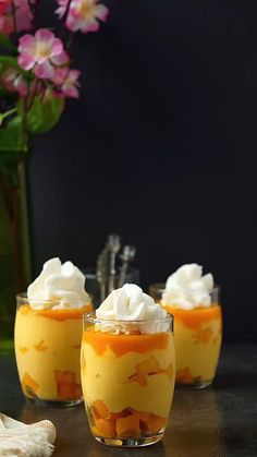 three desserts with whipped cream and orange sauce in small glass dishes on a table