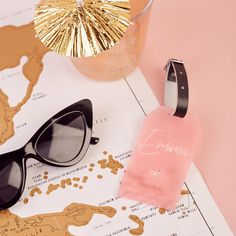 a pair of black sunglasses sitting on top of a map next to a pink bottle