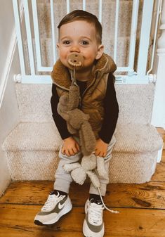 a young boy sitting on the steps with a pacifier in his mouth and wearing sneakers