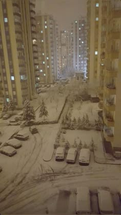 snow covered parking lot in front of apartment buildings at night with cars parked on the street