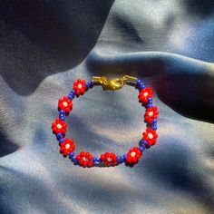 Red/Blue daisy chain bracelet with gold clasp. Red Bracelet Gift For Spring, Red Flower-shaped Jewelry For Spring, Red Flower Jewelry For Spring, Red Flower-shaped Spring Jewelry, Red Jewelry Spring Gift, Red Jewelry For Spring Gift, Red Summer Bracelet Jewelry, Red Bracelet Jewelry For Summer, Handmade Red Bracelets For Spring