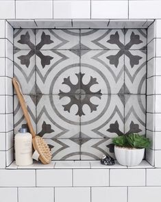 a white tiled bathroom with black and grey tiles on the wall, potted plants and a wooden spatula