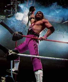 a man in pink pants standing on top of a wrestling ring holding a stick and rope