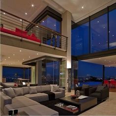 a living room filled with lots of furniture next to tall glass windows at night time