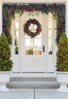 two white urns with christmas wreaths on them in front of a house door