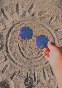 a person's hand holding up sunglasses in the sand with an imprint on it