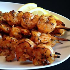 grilled shrimp skewers with lemon wedges on a white plate, ready to be eaten