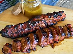 some meat is on a cutting board next to a jar of mustard and ketchup