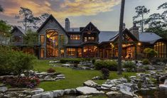 a large house surrounded by lush green grass and rocks with lights on the front windows