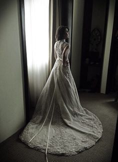 a woman standing in front of a window wearing a wedding dress