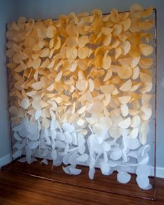 an art piece made out of white paper leaves on a wooden floor next to a wall