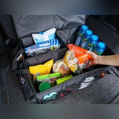 an open suitcase filled with food and drinks in someone's hand next to it