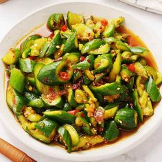 a white bowl filled with green vegetables covered in sauce on top of a marble table