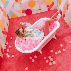 a woman laying in a bathtub filled with pink balls on top of a red carpet