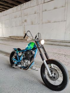 a blue and green motorcycle parked in front of a concrete wall with graffiti on it