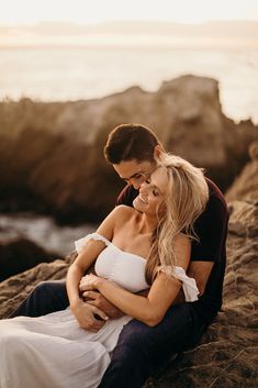 a man and woman are sitting on the rocks by the ocean with their arms around each other