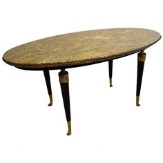 an oval marble table with black legs and gold trimmings on the top, against a white background