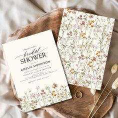 two wedding cards sitting on top of a wooden plate next to dried flowers and greenery