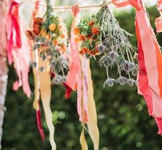 several ribbons hanging from a tree with flowers and leaves attached to the strings in front of them