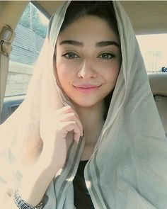 a woman in a car wearing a white shawl over her head and smiling at the camera