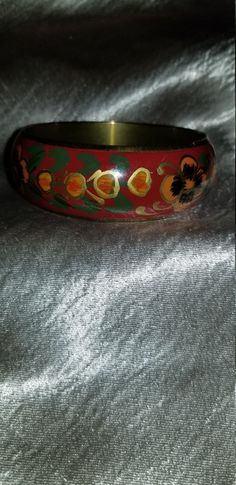 Thick Red floral enamel bracelet Enamel over brass with a red background and yellow and orange flowers with hints of gold and green leaves. Some tarnish on inside but otherwise in very good condition 2 1/2 In. inner diam best for a smaller wrist Just a teensy bit under one inch thick Vintage Red Round Bangle, Vintage Handmade Red Bangle, Red Hand Painted Jewelry For Festivals, Handmade Red Enamel Bracelets, Vintage Red Hand Painted Jewelry, Red Bangle For Formal Festivals, Red Enamel Bangle Bracelet, Red Enamel Bangle Bracelets, Yellow And Orange Flowers