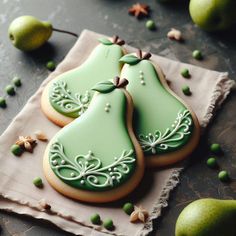 two decorated cookies sitting on top of a napkin next to pears and green leaves