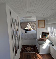 the inside of a camper with wood flooring and white walls, including a bed