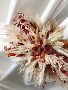 an arrangement of dried flowers and leaves on a white cloth