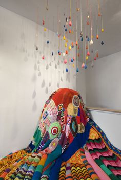 a multicolored blanket is draped in front of a white wall and hanging from the ceiling