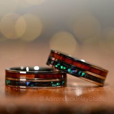 two wedding bands with green and red opal inlays sitting on top of each other