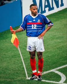 a soccer player standing on the field with his hands in his pockets and holding a flag