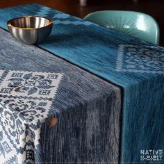 a blue table cloth with a silver bowl on it and two chairs in the background