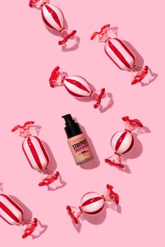 an image of cosmetics on pink background with red and white candies in the foreground