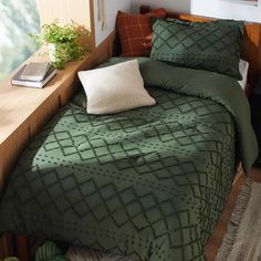 a bed with green bedspread and pillows in a room next to a window