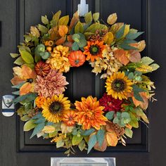 a wreath is hanging on the front door with autumn leaves and sunflowers around it