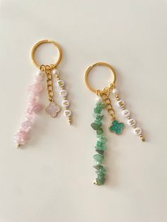 two key chains with charms attached to them on a white surface, one is gold and the other is green