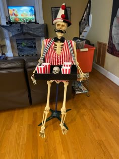 a skeleton sitting on top of a table with popcorn in it's hands and wearing a striped shirt