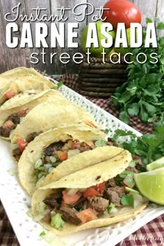 three tacos sitting on top of a white plate with limes and cilantro