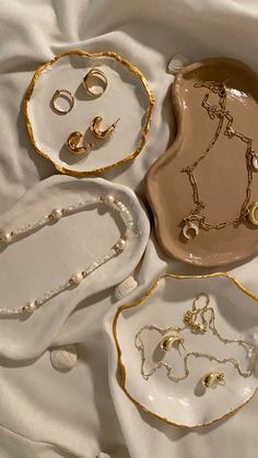 four pieces of jewelry sitting on top of a white cloth covered tablecloth with gold trimmings