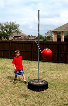 a young boy standing next to a red ball on top of a tire in a yard