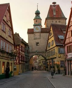 a cobblestone street lined with buildings and a clock tower in the background at sunset