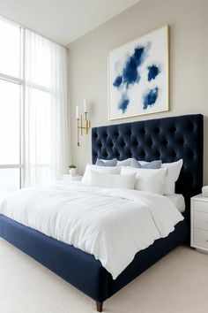 a bed with white sheets and blue headboard next to a painting on the wall