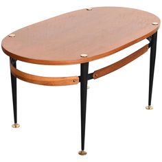 an oval wooden table with black legs and gold studdings on the top, against a white background