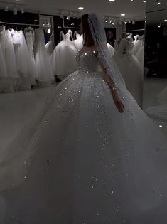 a woman in a wedding dress looking at dresses on mannequins behind her