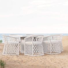 three white wicker chairs sitting on top of a sandy beach