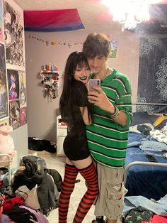 a young man and woman taking a selfie in a room with clothes on the floor