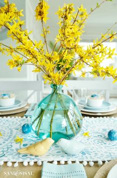 a vase filled with yellow flowers sitting on top of a table next to plates and napkins